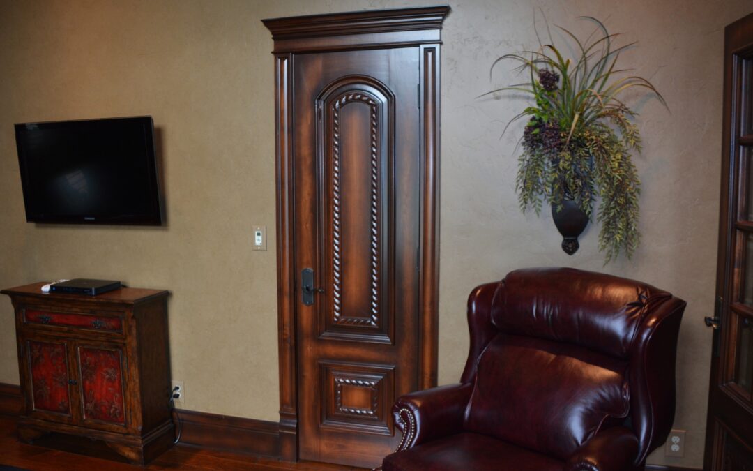 An entry way with a tall wooden door, a leather chair and a plant arrangement hangin g on the wall above it.