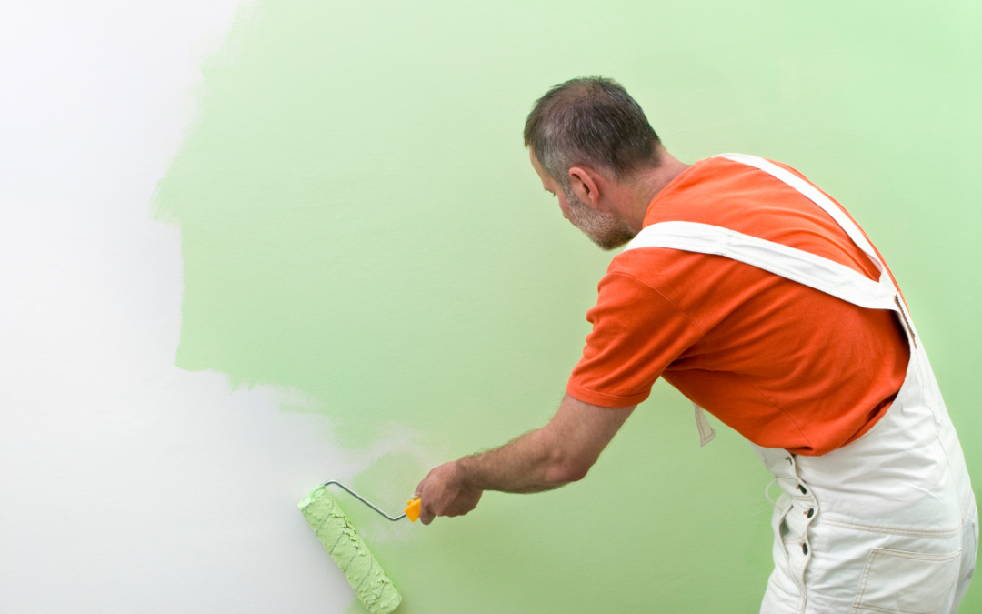 Painter in overalls painting a wall green