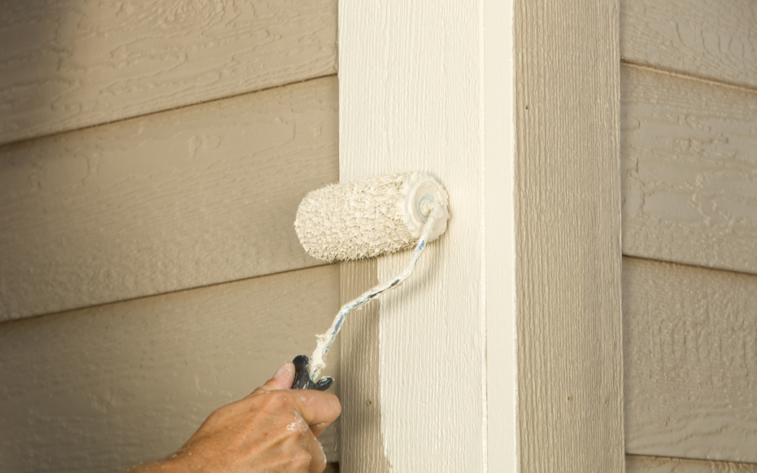 Someone using a paint roller on a house exterior