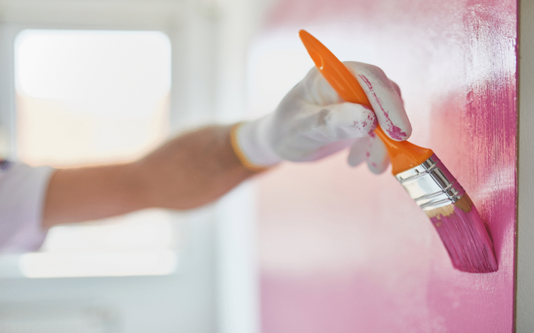 A close up of a paint brush painting a wall pink